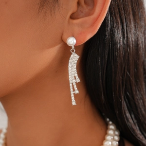 Detailed close-up of a silver tassel earring with a white pearl and sparkling rhinestones