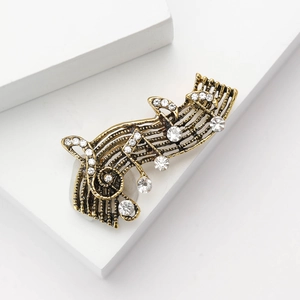 Vintage bronze music note brooch with crystals shown on geometric white pedestals
