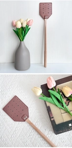Detail of durable leather fly swatter with long wooden handle in a minimalist home setting