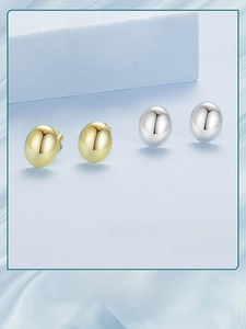 Detailed view of oval metal stud earrings in polished gold and silver finishes