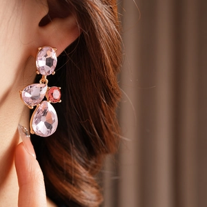 Close-up of vintage gold earrings featuring three tiered pink teardrop gemstones on model