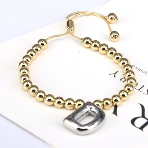 Detail view of golden beaded bracelet featuring a silver balloon letter D charm and adjustable cord