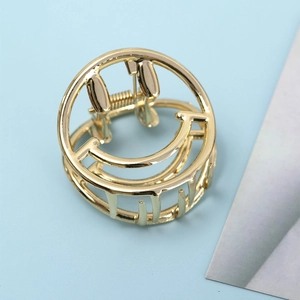 Minimalist gold metal hair claw clip featuring a hollow smiley face design on light blue background