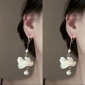 Long silver floral drop earrings with white shell pearls worn by a model
