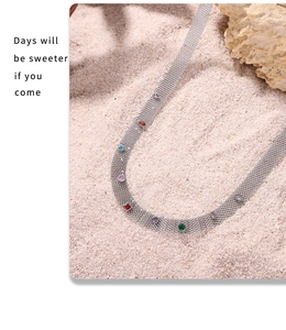 Detailed shot of mesh titanium steel necklace with colorful zircons on a sandy beach