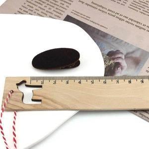 Close-up of a 4-5cm brown velvet hair clip measured on a wooden ruler on newspaper