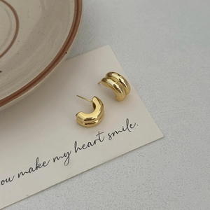 Close-up of double-layered C-shaped gold earrings placed on a cream artistic card