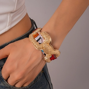 Detailed shot of a gold textured cuff bracelet intertwined with a colorful silk scarf