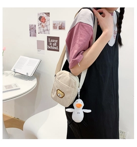Close-up of beige corduroy crossbody bag with brown bear embroidery and plush duck charm