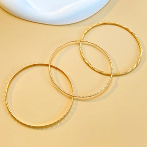 Detail of three slim gold bangles with geometric textured facets and polished finish