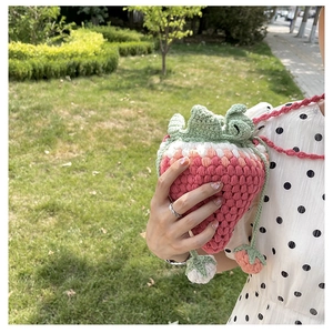 Close-up of handmade pink knit strawberry bucket bag with green leaf and woven strap
