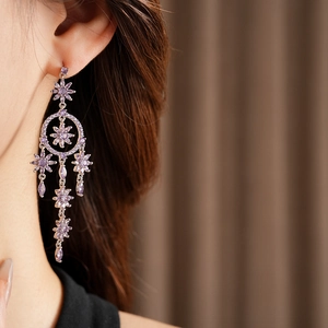Close-up of silver tassel earrings with purple floral crystals on a model