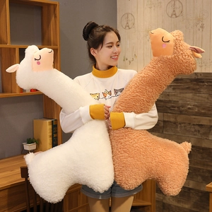 Detail view of large white and brown alpaca plush body pillows held by a model in a bedroom