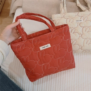 Close-up of quilted rabbit pattern and woven label on padded red and beige tote bags