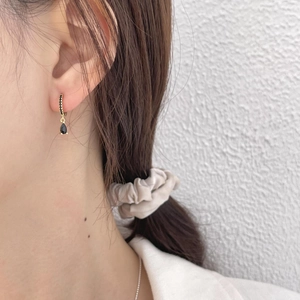 Model wearing a gold drop earring with black crystals and a pear-shaped gemstone pendant