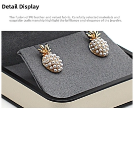 Macro shot of pineapple pearl earrings with gold details in a premium gray velvet jewelry box