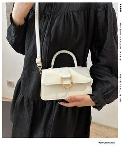 Detail of a creamy white patent leather crossbody bag with a large golden D-shaped buckle