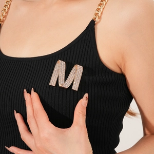 Detail of a sparkling crystal encrusted letter M brooch on a black knitted sweater