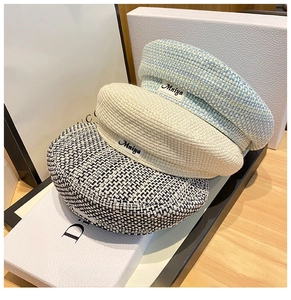 Close-up of stylish tweed beret with Mniya label in black, white, and teal colors