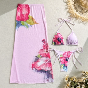 Flat lay of pink floral three-piece bikini set with a long mesh sarong and hibiscus prints