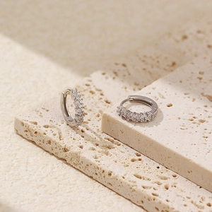 Macro detail of silver S925 hoop earrings with clear zircons on a textured stone