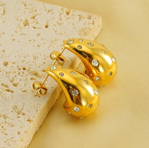Detail view of 18K gold teardrop earrings with sparkling zircons on a golden silk fabric