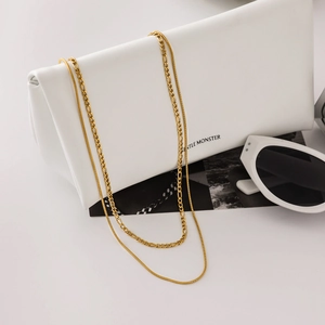 Detail of gold double-layered necklace featuring a snake chain and curb link over a white pouch