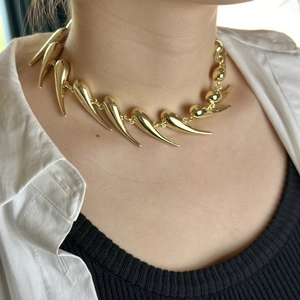 Close-up of a bold gold thorn necklace with sharp spike charms worn by a female model