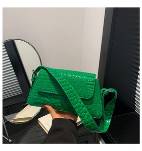 Detail of green crocodile embossed handbag featuring a stylish wide strap and glossy finish