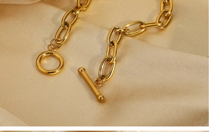 Close-up of gold-plated paperclip chain with OT toggle clasp on champagne silk fabric