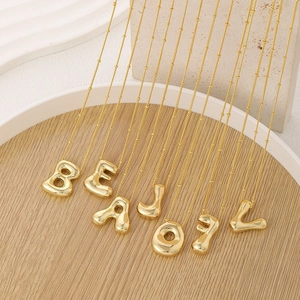 Detailed close-up of 18k gold plated bubble letter pendants on wooden display tray