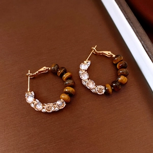 Close-up of golden hoop earrings featuring brown tiger eye beads and sparkling crystals