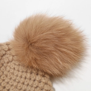 Close-up of caramel knit winter hat featuring a large fluffy faux fur pom-pom detail