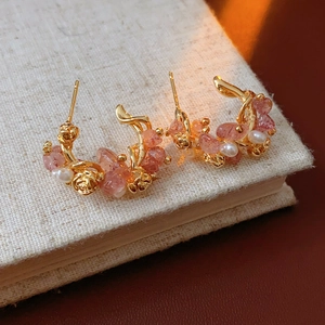 Close-up of gold plated hoop earrings with strawberry quartz and pearls on a book