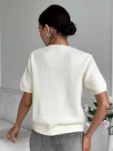 Dettaglio del retro del top in maglia color crema che mostra la trama del tessuto