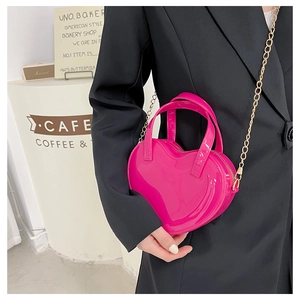 Close-up of heart-shaped hot pink jelly crossbody bag with gold chain strap on model