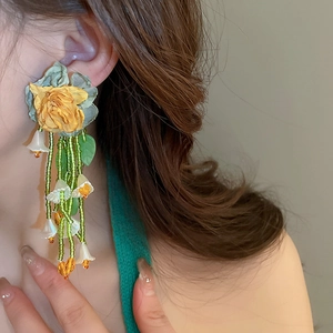 Gros plan de longues boucles d'oreilles à pompons verts et fleurs de muguet en tissu