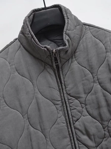 Detail of gray wave-quilted puffer jacket showing metal zipper and high-quality stitching