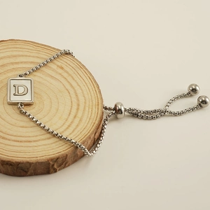 Adjustable stainless steel letter D bracelet with shell inlay on rustic wood background