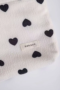 Close-up of white seersucker makeup bag featuring black heart prints and woven brand label