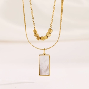 Double-layered 18k gold necklace with white mother-of-pearl rectangle pendant on beige fabric