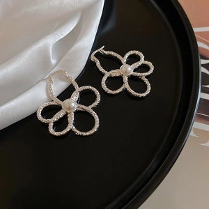 Macro shot of silver flower earrings with matte texture and a pearl center in the petal
