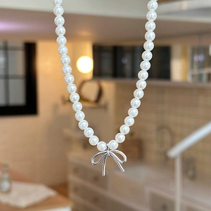 Detail of elegant white pearl necklace featuring a polished silver bow pendant design