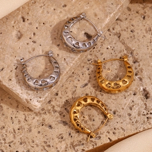 Detailed macro view of 18K gold and silver hollow heart U-shaped earrings on stone and silk