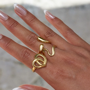 Close-up of gold stainless steel heart knot and wavy curve rings worn on female hand
