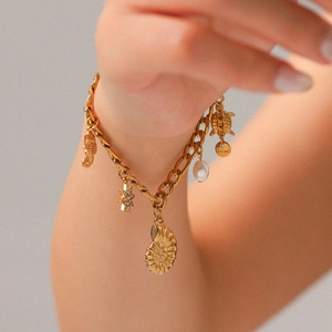 Detail of gold nautical bracelet featuring starfish, seahorse, turtle charms and a pearl