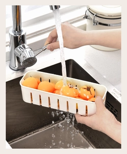Detail of white drainage basket for fridge storage showing water rinsing orange fruit