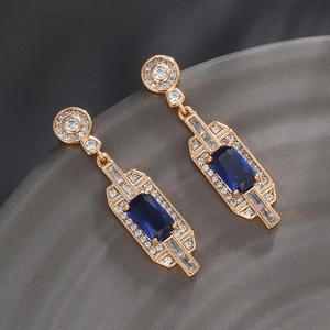 Macro detail of luxury gold-plated earrings featuring emerald-cut blue crystal stones