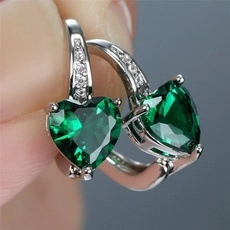 Macro shot of heart-shaped emerald green earrings held between fingers for size