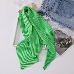 Detailed view of green pleated silk scarf on a white tray with lifestyle props